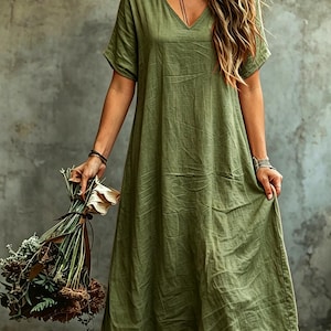 K&ouml;nnte beinhalten: Ein locker sitzendes, olivgr&uuml;nes Midikleid mit V-Ausschnitt und kurzen &Auml;rmeln. Das Kleidungsst&uuml;ck zeichnet sich durch eine strukturierte, leicht knittrige Stoffoberfl&auml;che und eine gerade, entspannte Silhouette aus, die unterhalb der Knie endet.