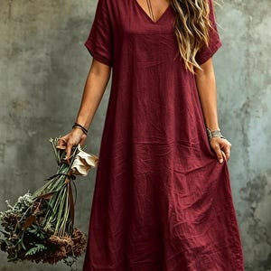 K&ouml;nnte beinhalten: Ein tiefburgunderrotes Midikleid mit V-Ausschnitt und kurzen &Auml;rmeln. Das Kleidungsst&uuml;ck hat eine lockere, weit geschnittene Silhouette mit einer strukturierten Stoffoberfl&auml;che. Das Kleid ist in einem einfarbigen Dunkelrot gehalten.