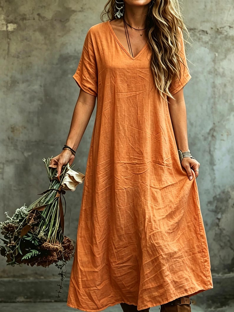 K&ouml;nnte beinhalten: Ein langes, locker sitzendes orangefarbenes Kleid mit V-Ausschnitt und kurzen &Auml;rmeln. Das Kleidungsst&uuml;ck hat eine texturierte, leicht knittrige Stoffoberfl&auml;che und reicht bis zur Waden- oder Kn&ouml;chell&auml;nge, was eine entspannte Silhouette ergibt.