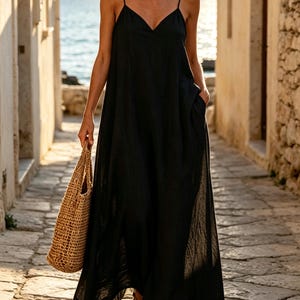 Pu&ograve; includere: Un abito lungo nero fino ai piedi con spalline sottili, scollo a V e tasche laterali. L'abito presenta una silhouette ampia e fluida ed &egrave; abbinato a una borsa tote in paglia intrecciata color marrone chiaro e sandali aperti.