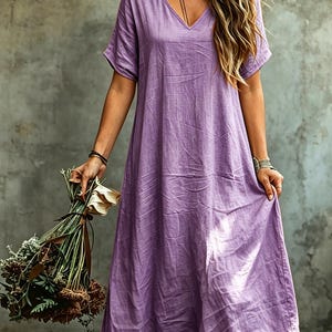 K&ouml;nnte beinhalten: Ein locker sitzendes, kn&ouml;chellanges Kleid in einem leuchtenden Lavendel-Lila. Das Kleidungsst&uuml;ck verf&uuml;gt &uuml;ber einen einfachen V-Ausschnitt, kurze &Auml;rmel und eine entspannte, flie&szlig;ende Silhouette mit einer strukturierten Stoffoberfl&auml;che.
