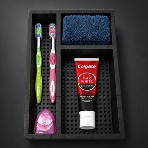 Peut inclure: Un plateau organisateur en mousse noire avec des sections perforées contenant une brosse à dents verte, une brosse à dents rose, un fil dentaire rose, une éponge bleue texturée et un tube de dentifrice Colgate Max White Charcoal.