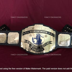 Puede incluir: Un cinturón de campeonato de lucha libre de cuero negro con una gran placa central dorada que presenta un gráfico de un globo terráqueo azul y el texto INTERCONTINENTAL HEAVYWEIGHT WRESTLING CHAMPION. Cuatro placas laterales doradas más pequeñas.