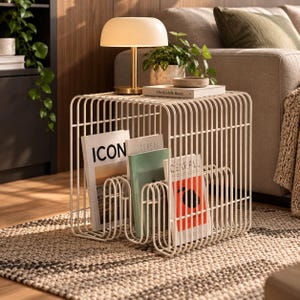 May include: A white metal side table constructed from vertical wire rods, featuring a built-in magazine rack base. The table holds three magazines titled ICON, CEREAL, and CEREAL, with a lamp and a book resting on its flat top surface.