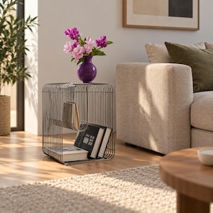 May include: A dark metal wire side table with a rectangular frame and vertical bars. The table features an integrated shelf holding three books and supports a purple glass vase filled with pink and purple flowers on its top surface.