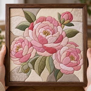 May include: A square fabric wall art piece featuring a quilted floral design of pink peonies and green leaves in a dark wood frame. The layered textile composition displays various shades of pink and green with intricate stitching details.