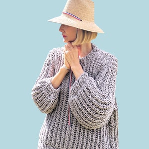 May include: A gray knitted sweater with a loose fit and long sleeves. The sweater has a ribbed texture and a round neckline.