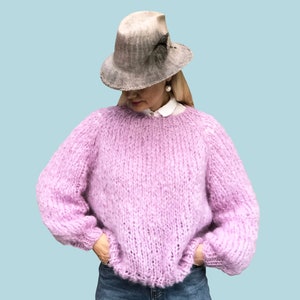 May include: A light purple knitted jumper with a round neckline and long sleeves. The jumper is made with a chunky yarn and has a relaxed fit.