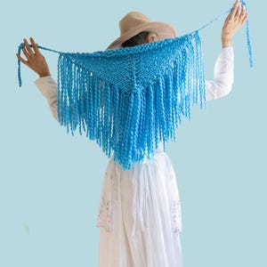 May include: A bright blue triangular knit shawl featuring long, thick fringe along the bottom edges. The word PATTERN is printed in white at the top, and the word BEGINNER is printed in blue at the bottom of this textile accessory.