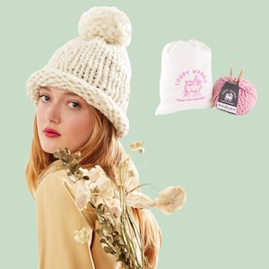 May include: A DIY kit for beginners featuring a cream-colored knit hat with a pom-pom, a bag of yarn, and a pink ball of yarn. The words "DIY KIT" and "ABSOLUTE BEGINNER" are displayed in the image.