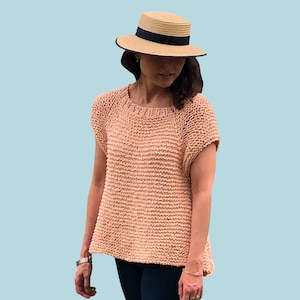 May include: A light peach-colored, short-sleeved knit top with a textured design. The top is paired with dark blue jeans. A straw hat with a black band is worn. The word "PATTERN" is displayed in white text.