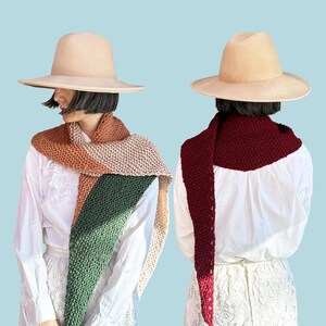 Op de afbeelding: Twee mensen dragen witte shirts en hoeden en dragen verschillende gekleurde gebreide sjaals. De sjaal links is een driehoekige sjaal in tinten groen, roze en bruin. De sjaal rechts is een lange, bordeauxrode sjaal met een kwast.