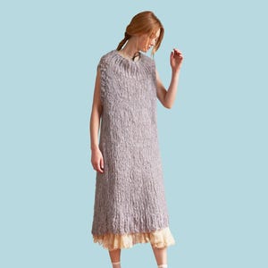 May include: A sleeveless, knee-length gray knitted dress with a textured appearance. The dress has a round neckline and a ruffled, cream-colored lace hem. The word "PATTERN" is displayed in a white rectangle above.