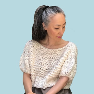 May include: A white knitted cropped sweater with short sleeves. The sweater has a loose fit and a slightly textured knit.