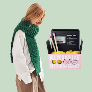 May include: A pink box with the text "All You Knit Kit My First Scarf" and a graphic of yarn balls, knitting needles, and a scarf. The box contains yellow yarn, knitting needles, and instructions for making a scarf. A person is wearing a green scarf.