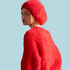 May include: A vibrant red knit beret and sweater set. The sweater has a textured, fuzzy appearance. The word "PATTERN" is displayed in a white rectangle at the top. The background is a light blue.