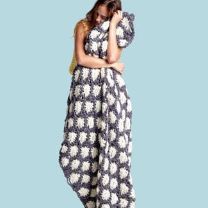 May include: A handmade, gray and white crochet blanket with a floral pattern. The blanket is draped over a person. The word "PATTERN" is in a white rectangle at the top of the image. The background is a light blue.
