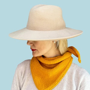 Peut inclure: Une femme portant un chapeau beige à larges bords et une écharpe en tricot jaune. L'écharpe est nouée à l'arrière du cou.