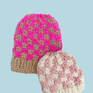 Op de afbeelding: Twee dikke gebreide mutsen. Eén is felroze en beige, de andere is roze en wit. Het woord "PATTERN" staat in een witte rechthoek bovenaan. De mutsen hebben een gestructureerd, geweven ontwerp, ideaal voor koud weer.