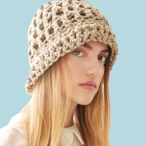 May include: A woman wearing a beige crochet bucket hat with a  "PATTERN" text overlay. The hat has a  crochet stitch pattern with open spaces.