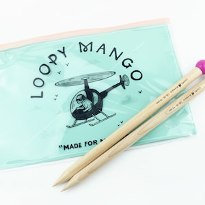 May include: Two wooden knitting needles with bright pink ball ends rest on a light blue plastic pouch. The pouch features the text "Loopy Mango" and a cartoon helicopter graphic. The needles are labeled "Loopy Mango US 19-15 mm".