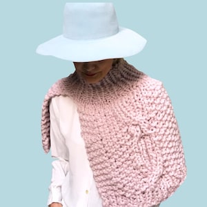 May include: A person wearing a light blue hat and a chunky knit scarf in a soft pink hue. The scarf is draped over a white shirt and blue jeans. The word "PATTERN" is in a white rectangle at the top.