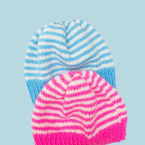 Op de afbeelding: Twee gebreide mutsen met horizontale strepen. De ene muts is lichtblauw en wit, de andere roze en wit. De randen van de mutsen zijn effen van kleur, waarbij de lichtblauwe muts een lichtblauwe rand heeft en de roze muts een roze rand heeft. Het woord "PATTERN" staat bovenaan.