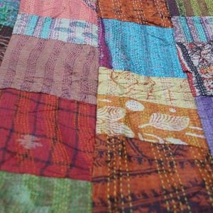 May include: A patchwork quilt featuring various rectangular fabric pieces in shades of red, orange, blue, green, and purple. The textile displays diverse patterns including floral, geometric, and abstract prints, all joined by visible white running stitch embroidery.