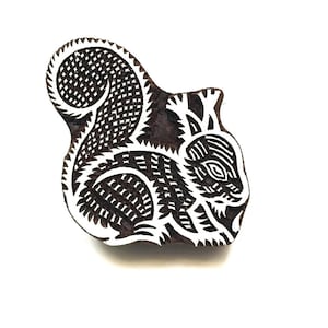 May include: A dark brown wooden printing block carved into the shape of a squirrel. The design features intricate white recessed lines forming the squirrel's fur, tail, and facial features, creating a high-contrast pattern for textile printing.
