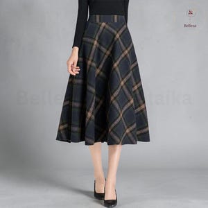 May include: A high-waisted midi skirt featuring a dark charcoal gray and forest green plaid pattern with thin tan diagonal lines. The skirt has a structured waistband and a flared, A-line silhouette that falls below the knees in a full shape.