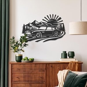 May include: A black metal wall art piece featuring a silhouette of a classic sports car driving on a winding road. The background includes a stylized mountain range, a dense forest of pine trees, and a rising sun with radiating beams.