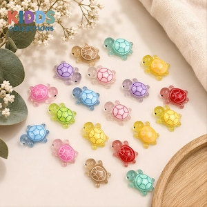 May include: A collection of small, translucent turtle-shaped charms in various colours including red, yellow, blue, green, pink, and brown. Each turtle features a distinct shell pattern with defined lines. The text KIDDS COLLECTIONS is visible.