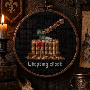 May include: A circular wooden embroidery hoop containing a cross-stitch design on black fabric. The design features a brown tree stump with a green and brown axe embedded in the top, accented with red stitching, and the text Chopping Block below.