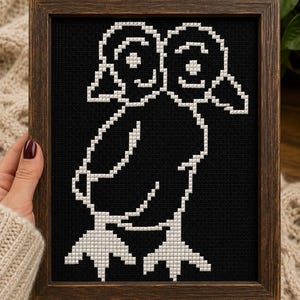 May include: A framed cross-stitch embroidery featuring a white two-headed bird silhouette against a solid black fabric background. The artwork is encased in a dark brown wooden frame with a simple, clean edge, highlighting the contrast of the design.