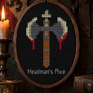 May include: A cross-stitch embroidery in a wooden hoop featuring a double-bladed axe with a brown handle and grey blades with red accents. The text Headman's Axe is stitched in white at the bottom against a black fabric background.