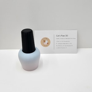 May include: A light blue and white gradient nail polish bottle holder with a black cap. Next to it is a white business card with the text Cat's Paw 3D, Family-Owned & Operated Print Shop, Find Us On Facebook, catspaw3d@yahoo.com, tiktok.com/@catspaw3d, and Houma, LA.