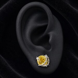 May include: A silver stud earring featuring a large, round, faceted yellow gemstone as the centrepiece. The setting is accented with small, clear stones and two star-shaped metal details along the edge, creating a celestial-inspired design.