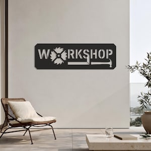 May include: A rectangular black metal wall sign featuring the word WORKSHOP in a stencil-style font. The letter O is replaced by a circular saw blade, and the letter P is formed by the shape of a hammer, with a square tool integrated below.
