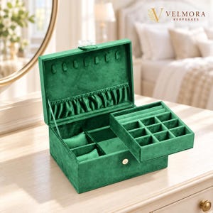 May include: A square emerald green velvet jewelry box with a gold-tone snap closure. The interior features a removable tray with nine small square compartments and two long slots, plus a bottom section with two watch pillows and open storage.