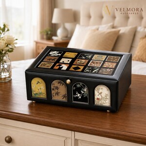 May include: A black rectangular storage box with a glass lid featuring a grid of twelve square panels with various nature-themed illustrations. The front panel has four arched windows displaying botanical and bird art with a small gold knob.