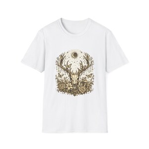 Może przedstawiać: Biały t-shirt z krótkim rękawem z centralnym nadrukiem graficznym w odcieniach brązu. Wzór przedstawia czaszkę jelenia z dużym porożem, otoczoną motylami, kwitnącymi kwiatami, grzybami oraz półksiężycem z gwiazdami powyżej.
