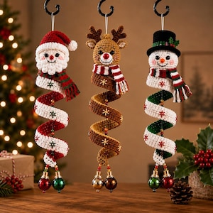 May include: Three hanging crochet ornaments featuring a Santa Claus, a reindeer, and a snowman. Each figure has a long, spiraling body decorated with small embroidered snowflakes, finished with two metallic jingle bells at the bottom.