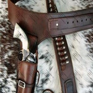 May include: A dark brown leather gun belt and holster set featuring a silver-toned buckle, multiple bullet loops containing metallic cartridges, and a single revolver with a light-colored grip secured within the holster.