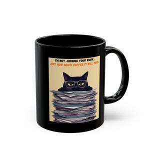 May include: A black ceramic mug featuring a graphic of a black cat wearing glasses, peeking over a large stack of papers. The text above the cat reads, "I'M NOT JUDGING YOUR WORK... JUST HOW MUCH COFFEE IT WILL TAKE." The mug has a curved handle.