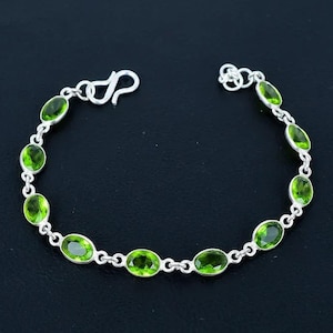 May include: A silver chain bracelet featuring ten oval-cut, faceted peridot gemstones set in individual silver bezels. The bracelet is connected by small silver links and includes a silver hook-style clasp at one end for secure fastening.