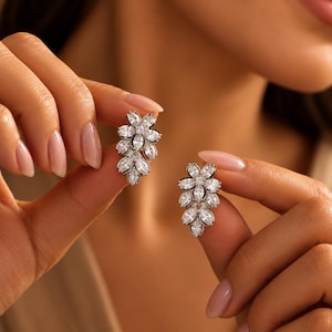 May include: A pair of silver-toned earrings featuring a cluster of clear, marquise-cut and round-cut stones arranged in a floral, leaf-like pattern. The stones are set in a metallic frame, creating a bright, reflective, and faceted appearance.