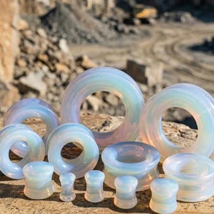 Puede incluir: Una colección de expansores y túneles para orejas iridiscentes y semitranslúcidos de varios tamaños. Estas piezas de joyería corporal circulares y lisas presentan un acabado lechoso y opalescente que refleja suaves colores pastel.