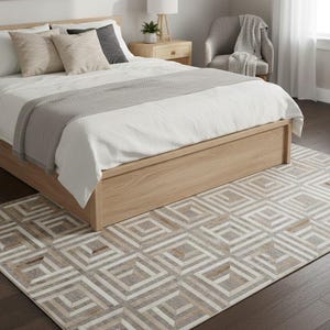 Op de afbeelding: Een rechthoekig vloerkleed met een geometrisch patroon van herhalende vierkanten in beige, grijze en witte tinten. Het kleed ligt op een donkere houten vloer onder een lichthouten bedframe, wit beddengoed en een grijze gebreide deken.