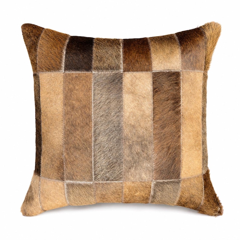 May include: A square throw pillow constructed from rectangular patches of genuine cowhide leather. The surface features a patchwork design with varying shades of brown, tan, and dark chocolate, showcasing the natural texture of the animal hair.