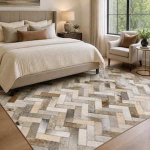 May include: A rectangular area rug featuring a herringbone pattern composed of individual cowhide patches in varying shades of cream, beige, tan, gray, and brown, creating a textured surface with natural hair-on-hide variations throughout.